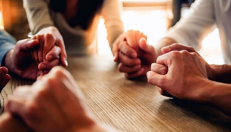 A group of people praying together, hands clasped